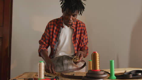 Fokussierter-Afroamerikanischer-Handwerker,-Der-In-Der-Lederwerkstatt-Mit-Werkzeugen-Einen-Gürtel-Herstellt