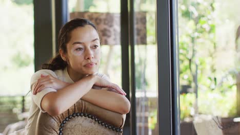 Thoughtful-biracial-woman-with-vitiligo-sitting-on-sofa-at-window-and-looking-outside