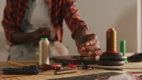 Hands-of-african-american-craftsman-wearing-apron-and-taking-tools-in-leather-workshop