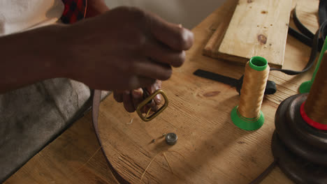 Hands-of-african-american-craftsman-using-tools-to-make-a-belt-in-leather-workshop