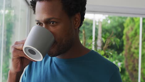Relaxed-biracial-man-drinking-coffee,-smiling-and-looking-into-distance