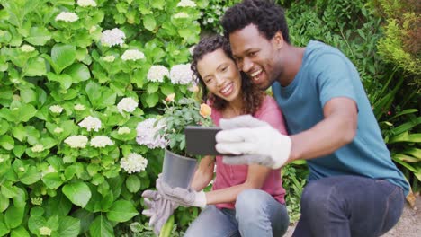 Feliz-Pareja-Birracial-Haciendo-Jardinería-Juntos,-Tomándose-Selfie-Con-Flores