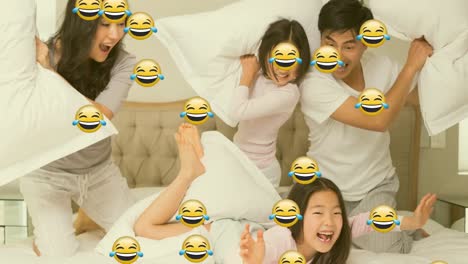 Animation-of-smiling-emoji-icons-over-asian-parents-and-two-daughters-pillow-fighting