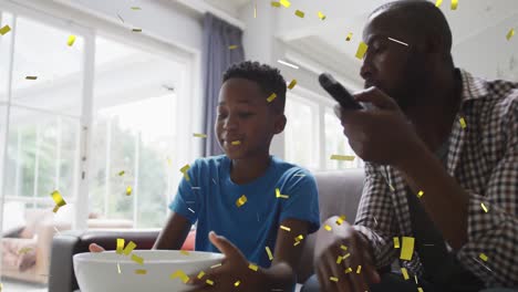 Goldenes-Konfetti-Fällt-Gegen-Afroamerikanischen-Vater-Und-Sohn,-Die-Sport-Im-Fernsehen-Schauen
