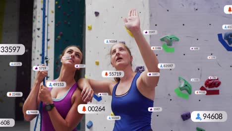Speech-bubbles-with-digital-icons-against-two-caucasian-fit-women-discussing-before-wall-climbing