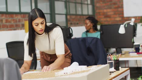 Thoughtful-biracial-female-architect-looking-at-architectural-models-at-office,