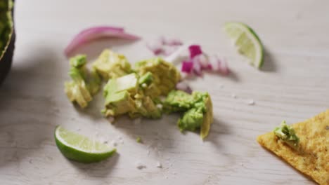 Video-of-tortilla-chip,-avocado,-onion-and-lime-on-a-wooden-surface