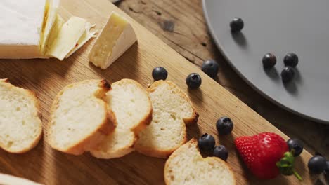 Video-of-slices-of-baguette,-bluberries-and-cheese-on-a-wooden-surface
