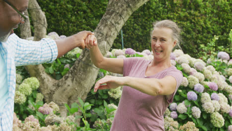 Happy-senior-diverse-couple-wearing-shirts-and-dancing-in-garden