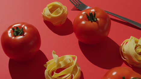 Video-Von-Frischen-Roten-Tomaten-Und-Nudelnestern-Mit-Gabel-Auf-Rotem-Hintergrund