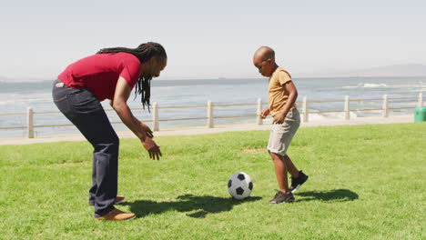 Video-Eines-Glücklichen-Afroamerikanischen-Vaters-Und-Sohnes,-Der-Draußen-Fußball-Spielt-Und-Spaß-Hat