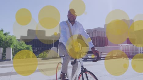 Animación-De-Puntos-Amarillos-Sobre-Un-Hombre-De-Negocios-Afroamericano-Montando-En-Bicicleta-En-La-Ciudad