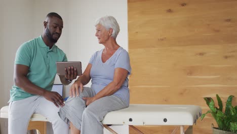 Video-of-african-american-male-physiotherapist-using-tablet-with-caucasian-senior-woman