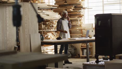 African-american-male-carpenter-talking-on-smartphone-in-a-carpentry-shop
