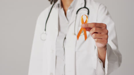 Video-of-smiling-biracial-female-doctor-holding-orange-kidney-cancer-ribbon