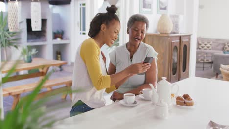 Afroamerikanische-Mutter-Und-Tochter-Lächeln,-Während-Sie-Zu-Hause-Gemeinsam-Das-Smartphone-Nutzen