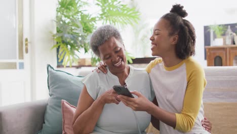 Afroamerikanische-Mutter-Und-Tochter-Lächeln,-Während-Sie-Zu-Hause-Gemeinsam-Das-Smartphone-Nutzen