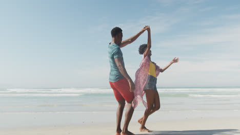 Happy-african-american-couple-dancing-and-holding-hands-on-sunny-beach