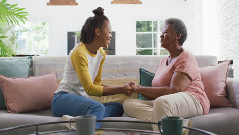 African-american-mother-and-daughter-holding-hands-and-smiling-sitting-on-the-couch-at-home