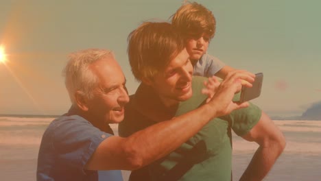 Animation-of-bokeh-over-happy-grandfather,-father-and-son-taking-selfie-on-beach
