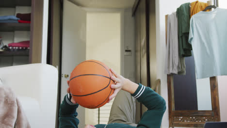 Asian-boy-playing-with-basketball-lying-on-the-floor-at-home