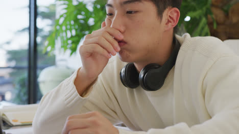 Asiatischer-Männlicher-Teenager-Mit-Kopfhörern,-Der-Im-Wohnzimmer-Lernt-Und-Einen-Laptop-Benutzt