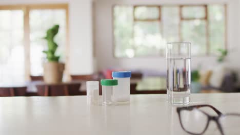 Close-up-of-boxes-of-pills-and-glass-of-water-with-glasses-on-table-in-living-room
