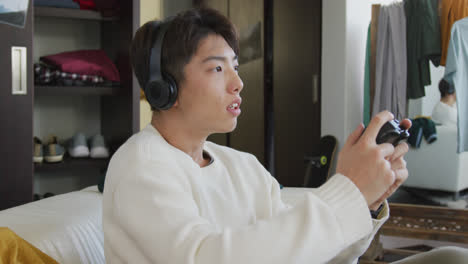 Asiatischer-Junge-Mit-Kopfhörern,-Der-Zu-Hause-Auf-Der-Couch-Videospiele-Spielt