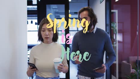 Spring-is-here-text-over-diverse-male-and-female-office-colleagues-discussing-in-corridor-at-office