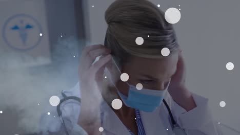 Animation-of-dots-white-over-caucasian-female-doctor-in-face-mask
