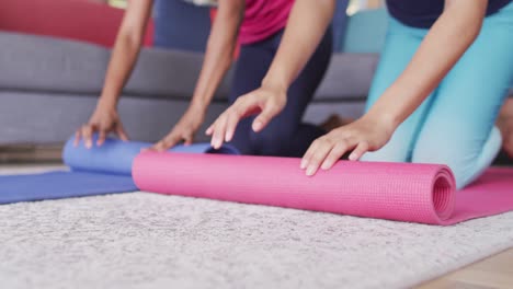 Video-of-midsection-of-diverse-female-friends-rolling-yoga-mats-at-home