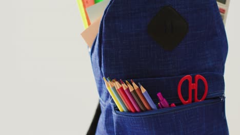 Video-of-backpack-with-crayons,-rulers-and-scissors-over-beige-background