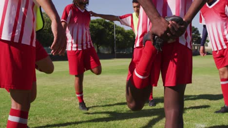 Video-Einer-Gemischten-Gruppe-Männlicher-Fußballspieler,-Die-Sich-Auf-Dem-Spielfeld-Aufwärmen,-Stehen-Und-Ihre-Beine-Ausstrecken