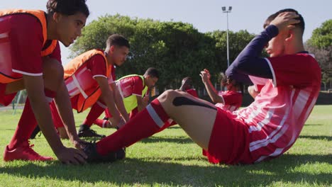 Video-of-diverse-group-of-male-football-players-warming-up-on-field,-doing-sit-ups