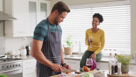 Video-of-happy-diverse-couple-preparing-meal,-drinking-wine-and-having-fun-in-kitchen