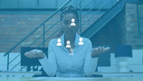 Animation-of-social-media-user-icons-over-african-american-woman-in-office-having-video-call