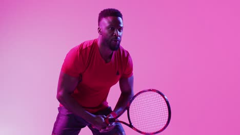 Video-of-focused-african-american-male-tennis-player-hitting-ball-on-neon-pink-lightning