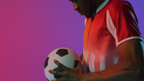 African-american-male-soccer-player-with-football-over-neon-pink-lighting