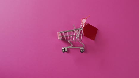 Video-of-shopping-trolley-with-red-price-tag-and-copy-space-on-pink-background