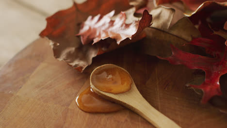 Video-of-maple-syrup-on-wooden-spoon-and-board-with-autumn-leaves