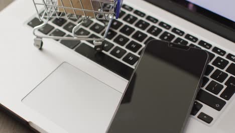 Boxes-in-shopping-trolley-and-smartphone-on-laptop-keyboard