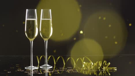 Video-of-two-champagne-glasses,-party-streamer-and-golden-glitter-on-black-background