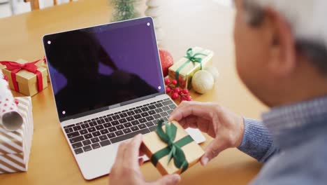 Video-of-senior-biracial-man-holding-gift-making-christmas-laptop-video-call,-copy-space-on-screen