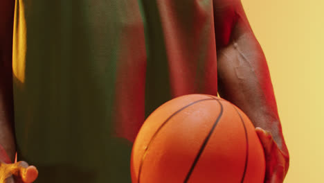 Video-Des-Mittelteils-Eines-Afroamerikanischen-Männlichen-Basketballspielers,-Der-Den-Ball-Auf-Orangefarbenem-Hintergrund-Hält