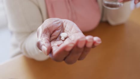 Senior-african-american-woman-sitting-at-table,-taking-pills