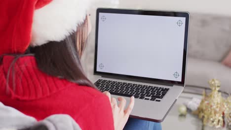 Biracial-woman-with-santa-hat-using-laptop-with-copy-space