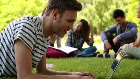 Student-using-laptop-and-classmates-speaking-behind-him