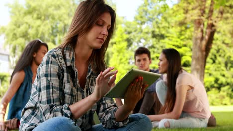 Student-using-tablet-and-classmates-speaking-behind-her-