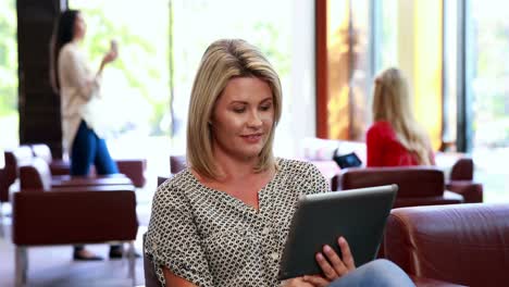 Focused-woman-using-her-tablet-while-smiling-at-camera