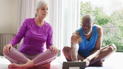 Happy-senior-diverse-couple-practicing-yoga-and-using-tablet